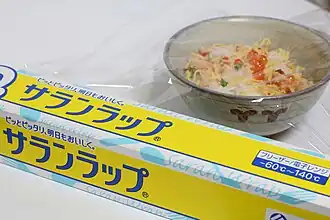 A film of plastic wrap is being used to cover a small bowl containing food.