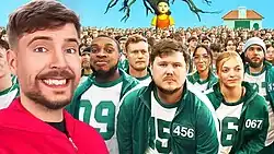 MrBeast stands left in a red jumpsuit with an excited expression on his face. Behind him is a crowd of people in green hoodies with numbered patches. Behind the crowd is a tree with no leaves and an animatronic girl taller than the crowd. To the right is a small house-like structure in the background.