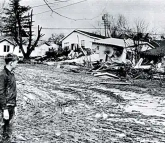 A destroyed home amidst a pile of rubble while a man looks on