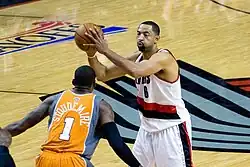 Howard is holding a basketball while a defender, with his back to the viewer, plays defense.