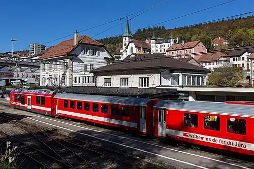 Red and white train at a train station next to a station building