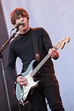 A brunette man playing the guitar and singing into a microphone while performing on stage.