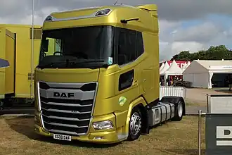 A yellow low-deck next generation DAF XG in a DAF stall at a truck show. It is a 2-axle chassis with dual tyres on axle two and a high capacity fuel tank.