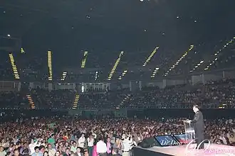 A man speaking to a large indoor audience