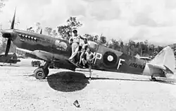 Black-and-white photo of a man wearing military uniform and two other men wearing only shorts standing on the wing of a single-engined monoplane aircraft