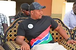 Talib Ahmed Bensouda wearing a shirt with the Gambia flag and a badge with the Kanifing coat of arms.