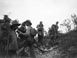 Soldiers wearing slouch hats and carrying rifles form up below a ridge line
