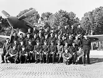 A group of uniformed men posing in front of a single-engined fighter plane