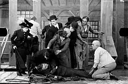 Film still of a man lying on the floor while several people try to attend to him