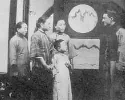 A black-and-white image of four people face-to-face with a man in glasses