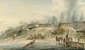 A forested coastline with several buildings, and two boats pulled up on the beach