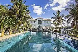A two-story house sits at the end of a palm tree-lined pool