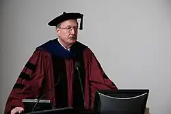 Middle-aged, bespectacled man in academic dress making a presentation