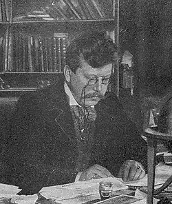 A middle-aged man in formal dress, using a monocle to read.