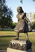 Bronze statue of a girl, apparently twirling about; the pedestal is decorated with characters from the "Alice" books by Lewis Carroll