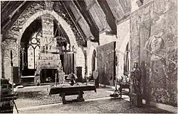 A monochrome photograph of a grand living room with a 36-foot-high arched ceiling, a high fireplace, and tall stained glass windows.