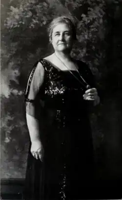 A middle-aged white woman, standing, wearing a dark sequined gown