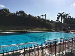 A view of a diving pool filled with water, and a railway embankment behind.