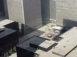 The plaza, as seen during the September 11 attacks in 2001. The elevated view shows the plaza facing the Marriott World Trade Center, and 1, 2, 3, 4 and 5 World Trade Center are visible. Debris is falling from the towers onto the plaza, which is strewn with debris. Many of the roofs of other buildings are also strewn with debris.