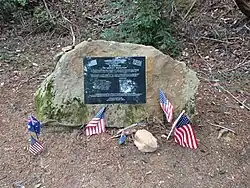 Photo of a memorial plaque fixed to a rock in El Corte de Madera preserve. Multiple small flags of the United States and Australia have been placed in front of it.