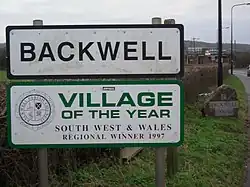 Road signs with Backwell in black writing on white background and below it another sign saying village of the year South West and Wales regional winner 1997.