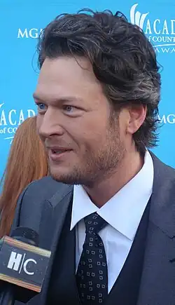 A man with black curvy hair smiling on a microphone