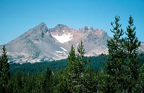 A volcano with a large crater rises above a forested region.