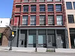 A view of a storefront with frosted windows, grey surround, and red brick building above.