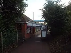 A red-brick building seen from a slightly higher elevation. There is an open space to walk through with a canopy above it. On the canopy there is a sign that reads "Brookmans Park". Both sides of the path are flanked by trees