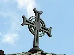 A metal cross affixed to a roof. It is composed of two crossed bars with a double concentric ring around the centre.