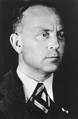 A black and white photograph, from the chest up, of a middle aged man wearing a suit