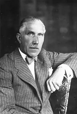 Portrait of an elderly man with grey hair and moustache in a pinstripe suit.