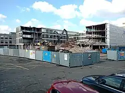 Fenced off site with four storey part demolished office type building having external cladding removed exposing metal framework