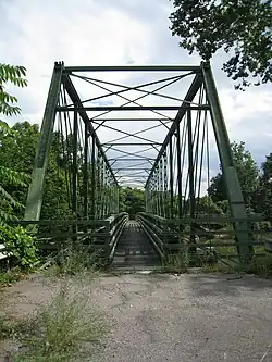 An image of the green Whipple truss bridge from along the side of a road