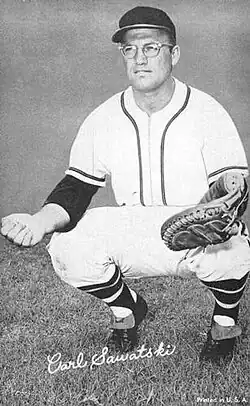 A man in a white baseball uniform squatting in preparation to catch a ball in his mitt.