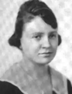 A young white woman with dark hair cut in a short bob with a bouffant crown; wearing a dark dress with a light collar