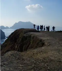 People standing on a coastal hilltop looking at islands