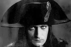 A monochrome photographic portrait of a handsome man in his late 20s wearing a French general's uniform from the 1790s and a cocked hat over stringy dark hair that reaches his shoulders