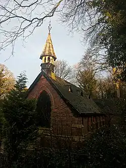 End view with large arched window and short spire in shadow against a pale sky