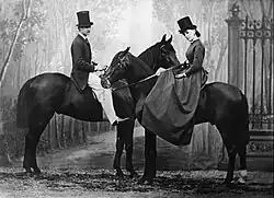 Black and white photograph of a woman and man on horseback against a studio backdrop