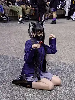 A young woman is cosplaying wearing cat ears and a school girl outfit and is posing for a photograph.