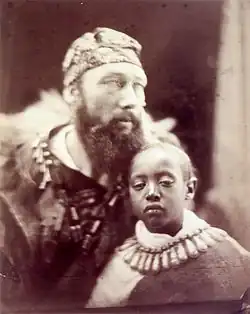 A black and white photograph of a man with a beard and a young boy, both wearing ornate clothing.