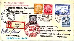 The reverse of a postcard. The consignee's address is in Buenos Aires, Argentina. It bears (on the right, above the address) 25 ℛ︁ℳ︁ worth of postage stamps and a special Deutsche Luftpost stamp for 2 ℛ︁ℳ︁. The stamps are cancelled by a postmark: "Berlin, 26.5.34", and a red cachet saying: "Deutsche Luftpost: Europa-Sudamerika" with a motif of a zeppelin and a Dornier Wal. On the left is the receiving postmark: "Buenos Aires, Argentina 31 May 1934"