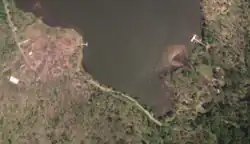 An aerial view of a forested area with a few buildings, showing trees blown down along a lakeshore.
