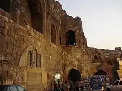 Cars and people in front of a stone wall with window and door openings and the remains of vaults