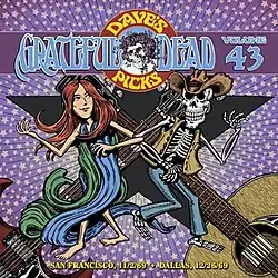 A woman wearing flowing robes dancing with a skeleton wearing cowboy clothes, with an electric guitar and an acoustic guitar in the background