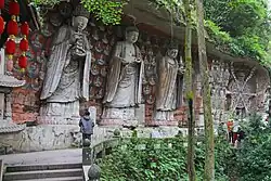 Several large Buddhist statues carved in a hill slope. Background is painted.