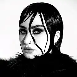 A black and white picture of Lovato looking into the camera with gelled strands of hair around her eye.