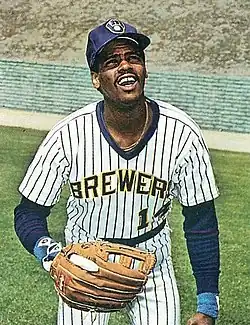 A man in a white baseball jersey with blue pinstripes and "Brewers" written across the chest wearing a fielding glove, prepared to catch a ball