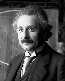Head and shoulders photo of Einstein with moustache and graying, curly hair, smiling slightly